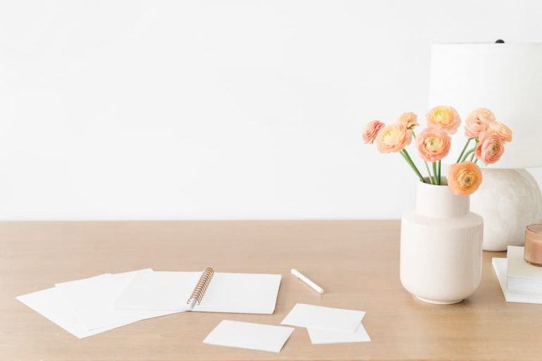 desk with paper clutter and a vase with flowers.
