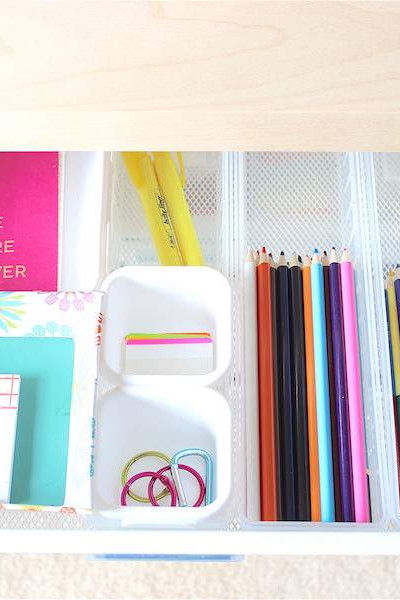 desk drawer filled with colorful office supplies organized with drawer dividers.