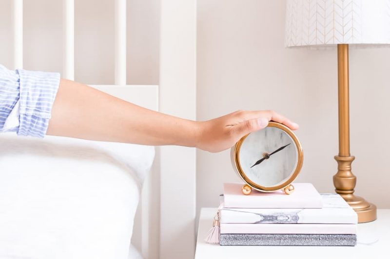 woman in bed hitting alarm clock.
