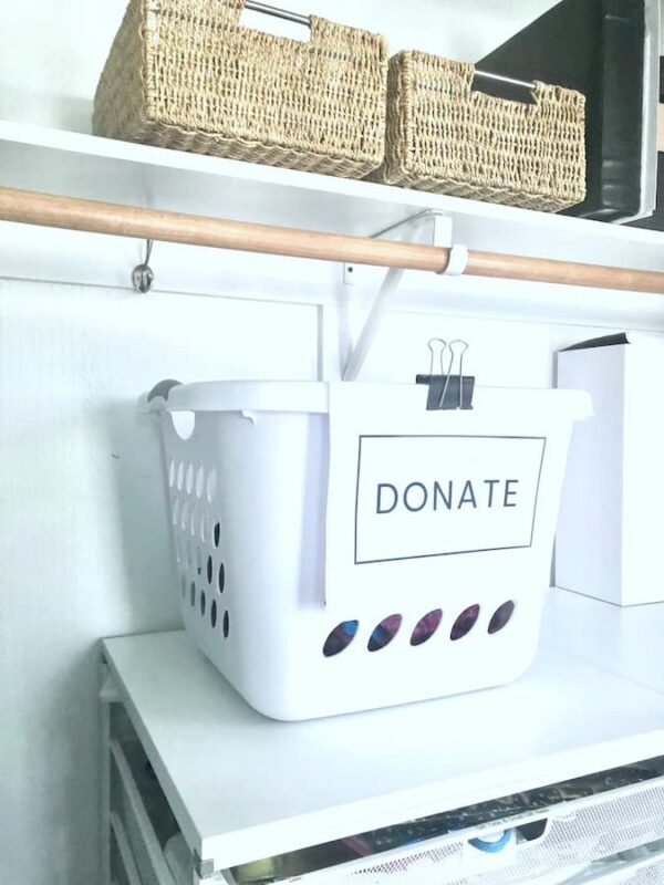 laundry basket with "donate" sign attached to it sitting on a shelf in a closet.
