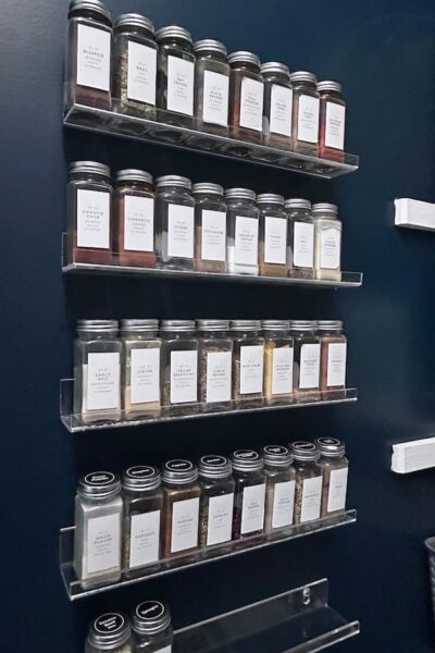 labeled spice bottles organized on acrylic shelves inside a pantry.